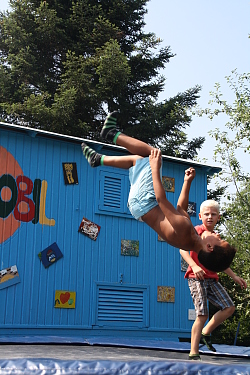 Das Bild zeigt zwei Jungen auf einem runden Trampolin vor dem Spielmobil. Einer der Jungen macht gerade einen Salto, der andere guckt zu.