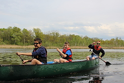 Das Bild zeigt drei Jungs in einem Kanu auf dem Wasser, der hinterste macht das Victory-Zeichen.