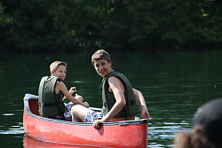 Das Bild zeigt zwei Jungen in einem Kanu, die sich nach hinten zu einem weiteren, nicht zu sehenden Kanu umdrehen.