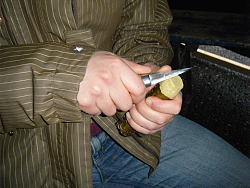 Das Bild zeigt Hände, die mit einem Messer an einem Stück dünnen Stamm schnitzen.