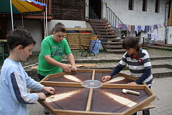 Das Bild zeigt drei Jungen, die an einem achteckigen Großbrettspiel spielen.