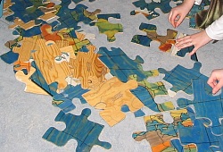 Das Bild zeigt Hände, die ein Riesen-Puzzle zusammenlegen. 