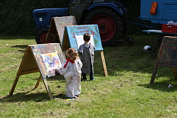 Das Bild zeigt zwei Kindern in Malerkittel an Holz-Staffeleien.